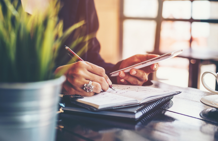 A lady looking at her phone and writing on a notebook