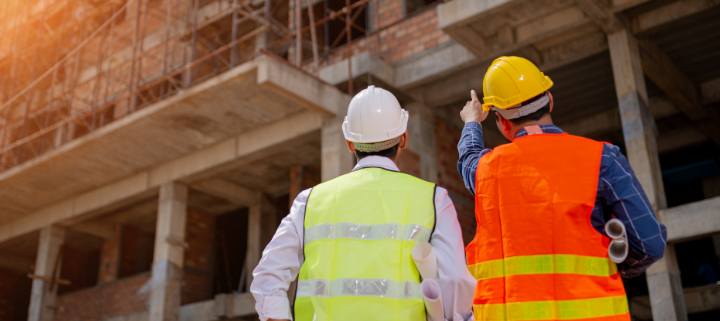 2 construction workers looking at a building and talking